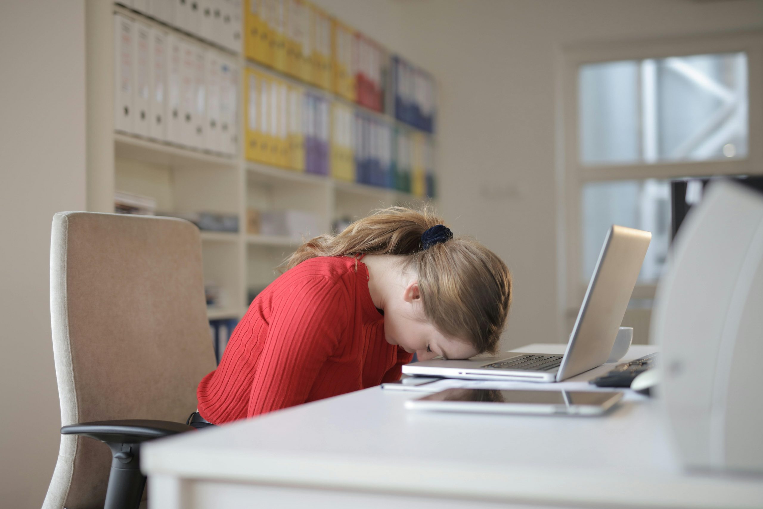 frustrated woman with her head on her laptop, sitting at a desk